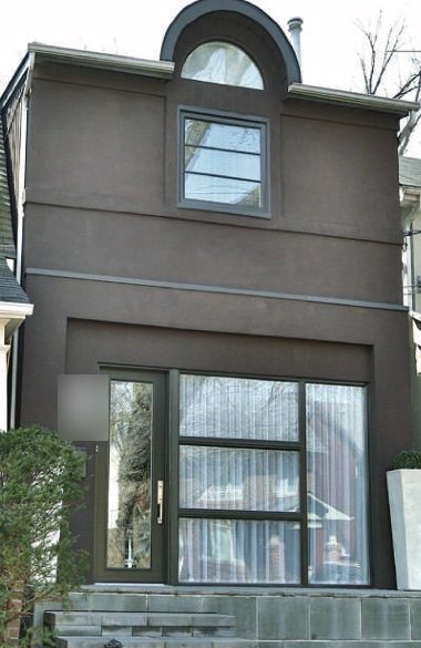 The completed facade with a dark stucco finish, a framed window and a new entrance